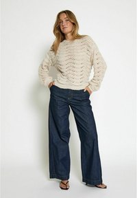 Cream-colored knitted sweater with wave patterns, paired with high-waisted dark blue wide-leg jeans and black sandals.
