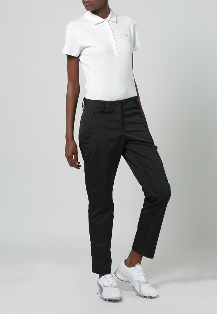 Vit polo med krage och logotyp, ihopparat med svarta avsmalnande byxor. Skorna är vita sneakers med grå detaljer.