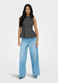 Grå peplum-top med lodrette sømme, parret med løse lys blå brede bukser. Modellen bærer teal højhælede sko.