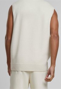 Pull sans manches en maille crème clair, tissu en mélange de coton avec une texture douce. Ourlet et emmanchures côtelés. Design simple et épuré.