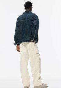 Jeans jakna v temno modri barvi z oblikovanim ovratnikom, kombinirana s kremnimi cargo hlačami, ki imajo več žepov in sproščen kroj.