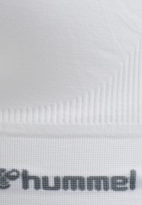 Close-up van wit gestructureerd textiel met ribbels en een gedeeltelijk zwart "hummel" merklogo aan de onderrand.