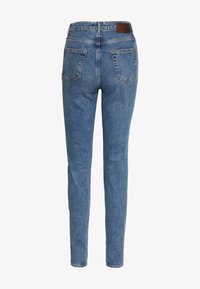 Slimmade blå denimjeans med en slät textur, hög midja och två bakfickor. Har en brun läderpatch vid bakre midjan.