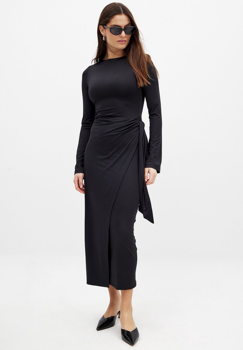 Black long-sleeve wrap dress in stretchy material, featuring a side tie detail and a fitted silhouette that falls to mid-calf.