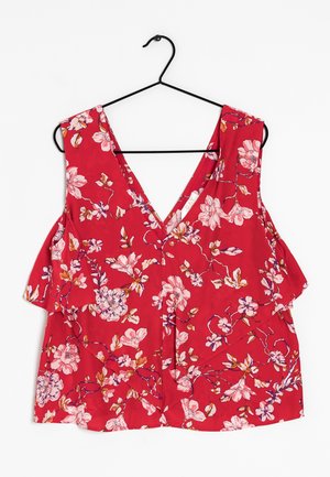 Blusa sin mangas roja con estampado floral rosa y blanco colgada en una percha negra sobre fondo blanco.