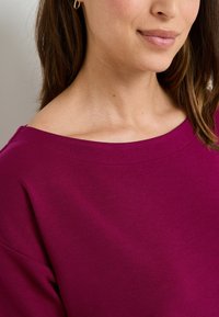 Pull bordeaux avec un large col et un tissu doux et texturé. Présente des coutures propres et des manches courtes, mettant en valeur une coupe décontractée.