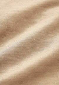 Tissu beige avec une surface lisse et subtilement texturée. Le matériau semble léger et légèrement brillant, avec un motif de tissage fin.