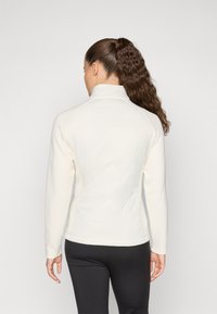 Leichte Cremejacke mit hohem Kragen, gerippter Textur an den Ärmeln und einem gesteppten geometrischen Design auf dem Rücken.