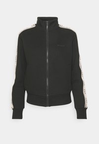 Veste noire zippée avec col montant et bande blanche ornée de logos courant le long des deux manches.