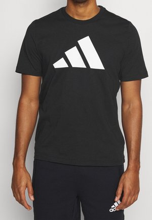 Hombre con camiseta Adidas negra con gran logo blanco de Adidas y pantalones cortos negros con pequeño logo blanco de Adidas en la pierna izquierda.