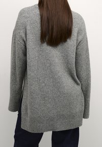 Pull gris en maille avec une coupe décontractée, ourlet côtelé et manches longues. Texture douce, légèrement plus long à l'arrière, mettant en valeur un design décontracté.