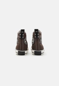 Braune Canvas-Halbsneaker mit weißen Nähten, schwarzen Akzenten und runden Logo-Patches. Gummisohlen und strukturierte Fersendetails.