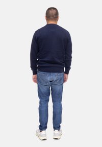 Maglione a maglia blu navy, design casual, polsini a costine, abbinato a jeans azzurri chiari e sneakers grigie con dettagli bianchi. Vista da dietro.