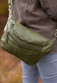 Borsa a tracolla in pelle verde oliva con più scomparti con zip, texture liscia e tracolla regolabile. Nessun logo o motivo visibile.