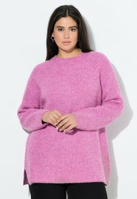 Rosa stickad tröja med ribbat mönster, med rund halsringning, ledig passform och sidofickor, kombinerad med mörka byxor.