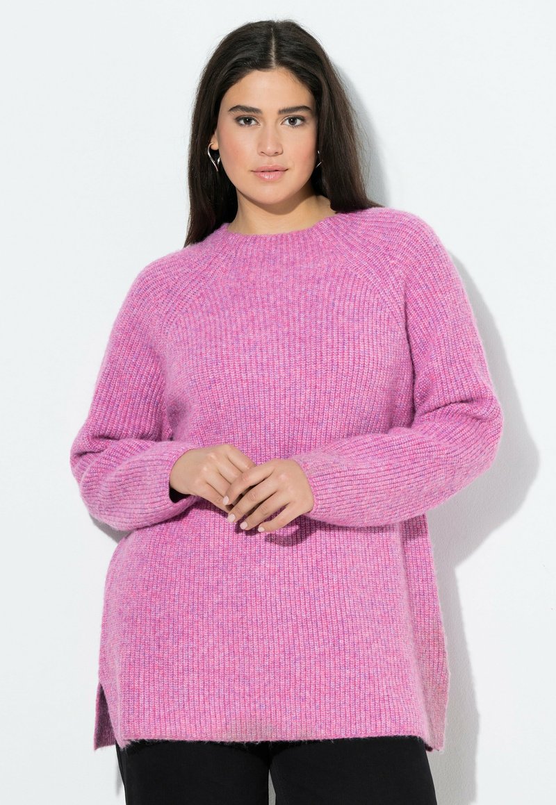 Rosa stickad tröja med ribbat mönster, med rund halsringning, ledig passform och sidofickor, kombinerad med mörka byxor.