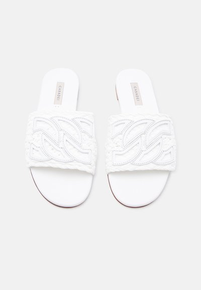 Λευκές επίπεδες σαγιονάρες με πλεκτούς ιμάντες που διαθέτουν ενωμένο καμπύλο μοτίβο και το όνομα της μάρκας εμφανές στα πέλματα.