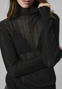 Schwarzer gerippter Rollkragenpullover mit leicht transparenter Textur, langen Ärmeln und lockerer Passform, der in einer Nahaufnahme ein geschichtetes Design zeigt.