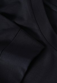 Tissu de coton bleu marine foncé avec une texture lisse, présentant un éclat subtil et des coutures soignées le long des coutures et du col.