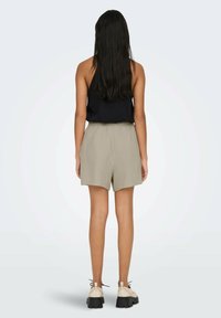 Light beige shorts with a textured pattern, elastic waistband, and a relaxed fit, paired with a black sleeveless top and cream-colored shoes.