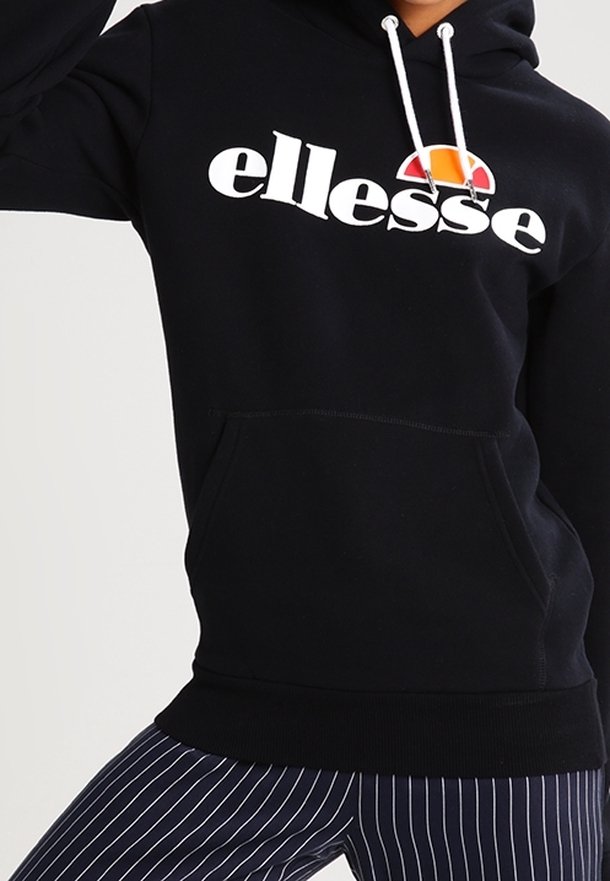 Sweat à capuche noir avec le logo "ellesse" blanc, doté d'une poche kangourou à l'avant, d'une capuche avec cordon de serrage, et de poignets et ourlet côtelés. Associé à un pantalon rayé.