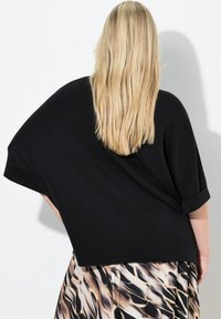 Maglia nera oversize con maniche corte arrotolate, caratterizzata da una texture liscia. Indossata con tessuto fluente e stampato in tonalità beige e marrone.