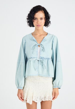 Lichtblauwe denim blouse met lange mouwen, strik voorkant en cinched taille. Gecombineerd met een witte kanten rok met een gerimpelde zoom.