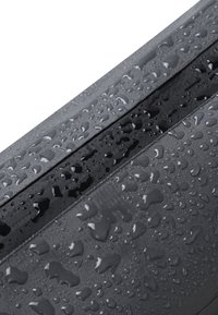 Tessuto nero idrorepellente con gocce, caratterizzato da una texture liscia e due cuciture parallele. Accenti di grigio scuro brillano attraverso l'umidità.