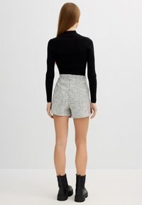 Top negro de manga larga acanalado combinado con pantalones cortos grises de alta cintura y textura, complementado con botas negras hasta el tobillo con suela gruesa.