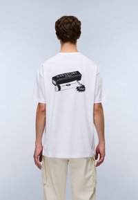 Hvid t-shirt med korte ærmer har en grafisk design på ryggen, der viser en sort-hvid spraydåse med "NAPAPIJRI" tekst og stjerneaccenter.
