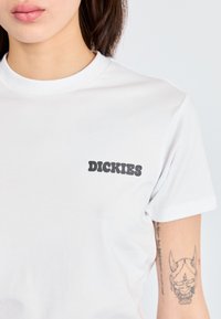 Balta medvilninė marškinėlių bei juodas "DICKIES" logotipas kairiajame krūtinės kampe. Klasikinis apvalus kaklas ir trumpi rankoviai. Lygi tekstūra.