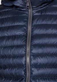 Navy pufferväst med horisontellt quiltat mönster, med en grå dragkedja i full längd och en huva. Slät, glänsande yta.