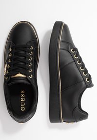 Sneaker basse in pelle nera con lacci neri, occhielli dorati, bordino dorato lungo le suole e targhetta dorata con logo sulla linguetta.