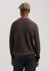Brun ribbestrikket genser med rund hals; modellen har på seg en tan flat cap; glatt tekstur med lange ermer og avslappet passform.