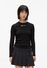 Czarny, długi rękaw, prążkowany top z okrągłym dekoltem i białym logo "KARL LAGERFELD JEANS". Połączony z plisowaną czarną mini spódniczką z bocznym sznurowaniem.