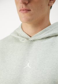 Lys grå sweatshirt med hætte, prydet med et hvidt Jumpman-logo på brystet. Lavet af blødt stof med en glat tekstur.
