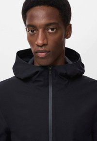 Črna zip-up jakna s kapuco, ki ima gladko teksturo in kontrastni sivi zadrgo. Detajl slikane modele, ki nosi jakno.