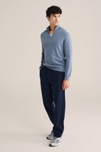 Világoskék zip-nyakú pulóver, sötét tengerészkék nadrág és szürke sportcipő. Simább anyag, laza fazon, laza stílus, egyszerű, tiszta megjelenéssel.