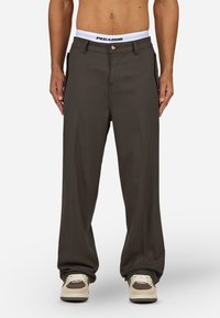 Brązowe spodnie o szerokich nogawkach, wykonane z gładkiego materiału, z zapięciem na zamek i guzik, białym, markowym pasem oraz bocznymi kieszeniami.
