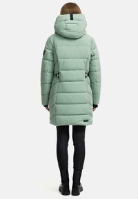 Mint green puffer coat with a hood, quilted design, black hardware accents, and adjustable waist features. Worn over black pants and boots.