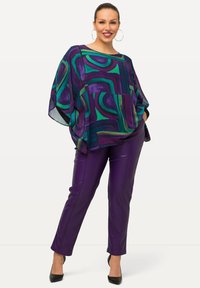 Tvådelat outfit med en multikolor geometriskt mönstrad genomskinlig topp i lila, grön och blå, som matchas med figurnära lila fuskskinnbyxor.