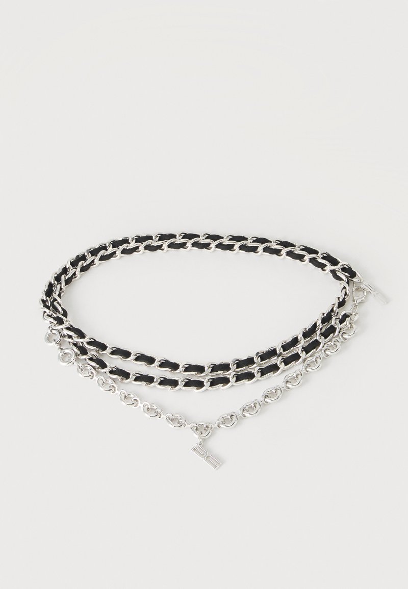 Ceinture double chaîne en argent avec détail en cuir tressé noir et petit pendentif métallique rectangulaire sur fond blanc.