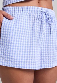 Shorts în carouri albastre deschise și albe, cu talie elastică și șnur. Materialul pare moale și ușor, având o croială lejeră.