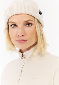 Creme fleece top med lynlås-kant, med et diskret logo. Sammen med en ribbet beige strikket hue, der fremhæver tekstur og design detaljer.