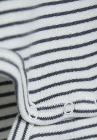 Pasiasty strój z białymi i granatowymi poziomymi liniami, wykonany z miękkiego materiału o gładkiej strukturze, z zatrzaskami u dołu.