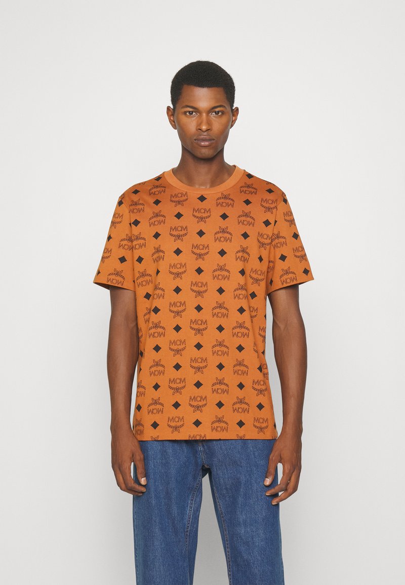 Orange kortärmad t-shirt med ett mönster av svarta logotyper över hela, rund halsringning och en slät bomullstextur. Avslappnad passform.