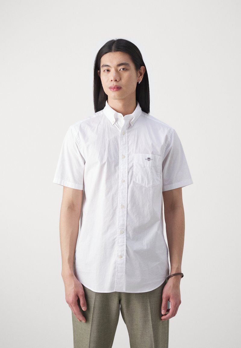 Chemise blanche à manches courtes, boutonnée, en coton, dotée d'une poche poitrine, avec un petit logo au-dessus de la poche et un col classique.