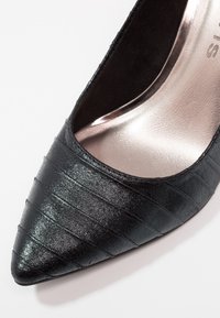 Chaussure femme noire à bout pointu avec motif à rayures horizontales texturées et semelle intérieure métallique.