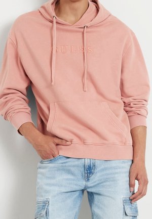 Sudadera rosa claro hecha de tela suave, con un bolsillo canguro frontal y cordones, con "GUESS" bordado en el pecho.