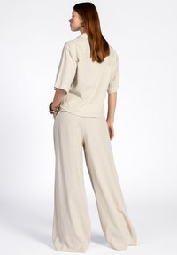 Ensemble en lin deux pièces de couleur beige clair, comprenant un haut à manches courtes avec col et un pantalon à jambes larges. Texture lisse et coupe décontractée.